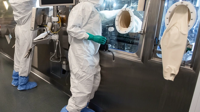 Two associates in full personal protective equipment stand at the production line